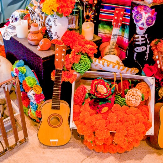 An ofrenda banked with marigolds and sugar skulls, a guitar leaning against the table.
