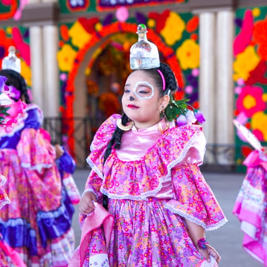 A young dancer in a pink embroidered dress and beaded crown waiting to perform.